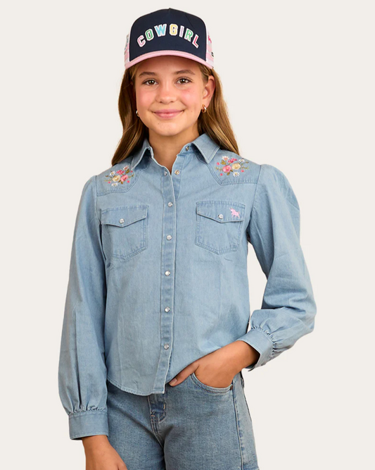 Girl wearing a denim shirt and shorts with a 'Cowgirl' cap on a white background