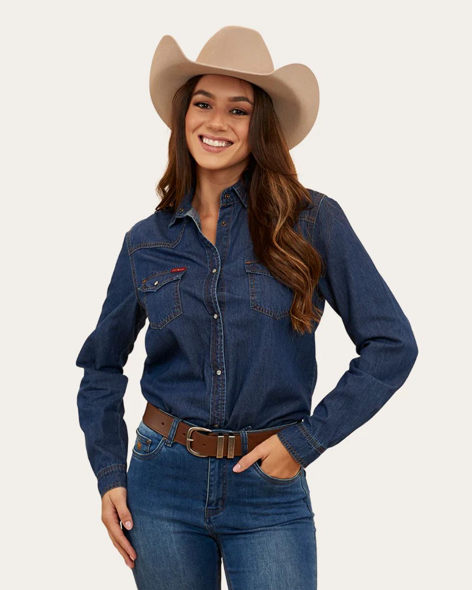 Woman wearing a blue denim shirt, jeans, and a beige cowboy hat on a light gray background
