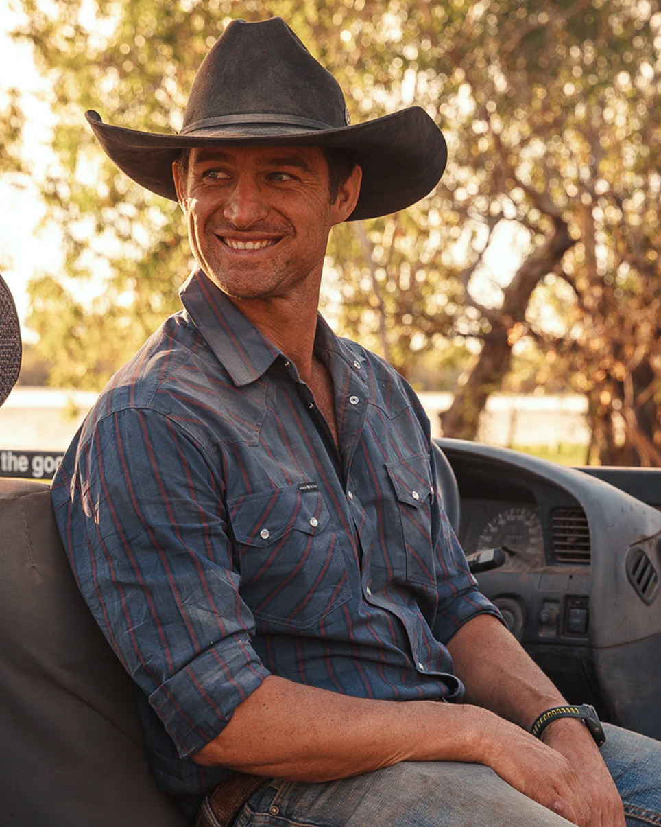 Man wearing a cowboy hat and blue shirt sitting in a vehicle with a blurred natural background