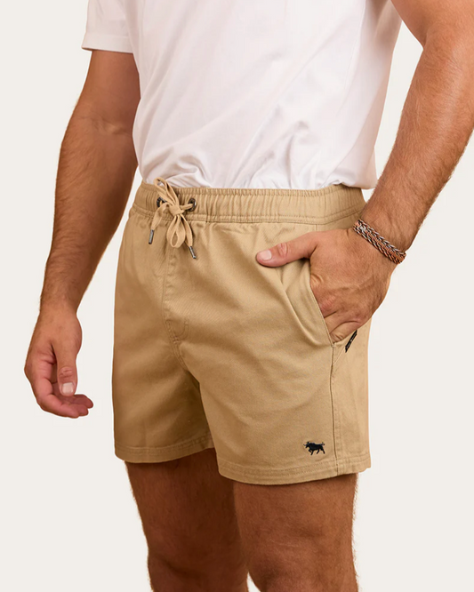 Person wearing beige shorts with a small logo on a plain background