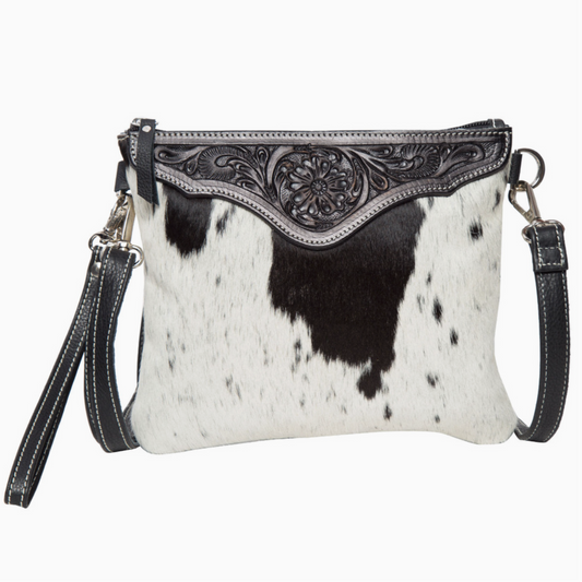 Cow print handbag with intricate black leather flap on a white background