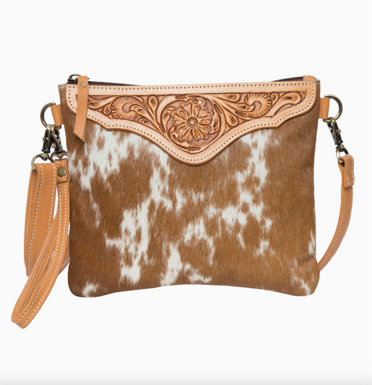 Brown and white cowhide patterned handbag with decorative flap on a white background