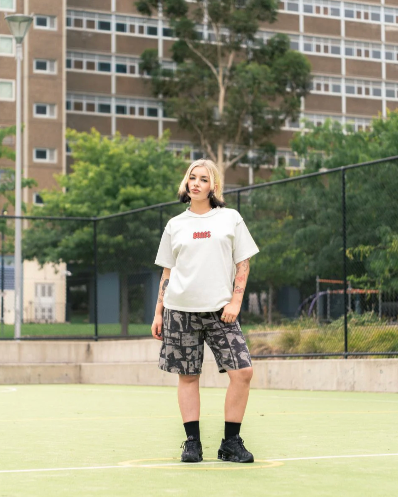Person wearing a white t-shirt with text and camouflage shorts on a tennis court.