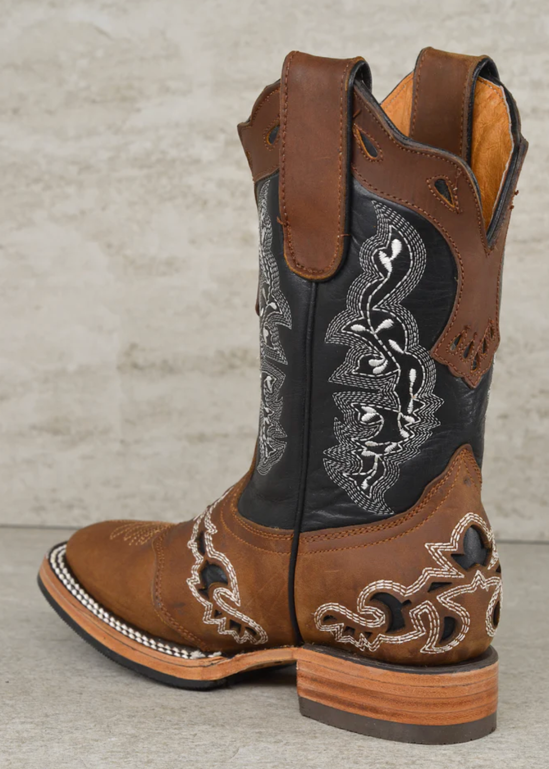 Brown cowboy boot with intricate black and white embroidery on a gray background