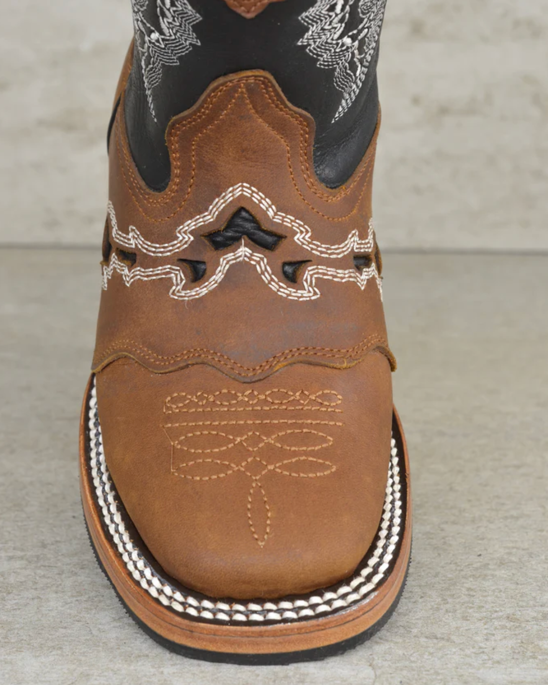 Brown cowboy boot with intricate stitching on a gray background