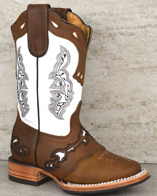 Brown and white cowboy boot with intricate designs on a textured surface