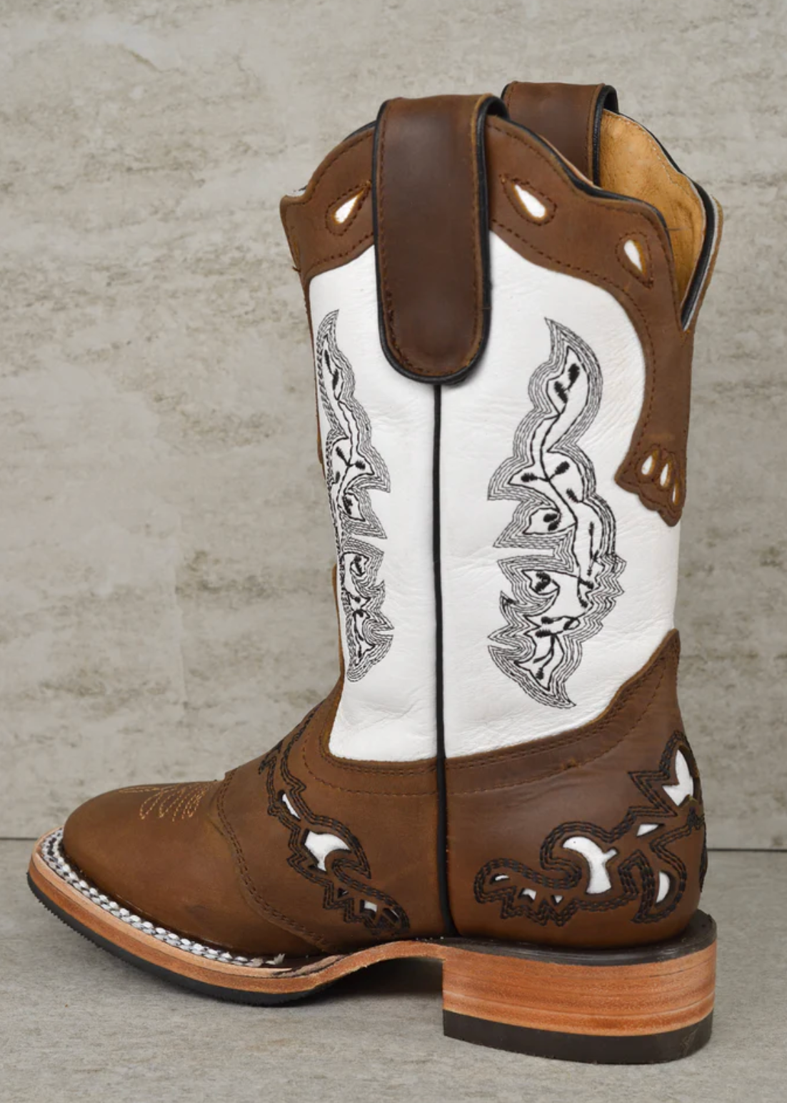 Brown and white cowboy boot with intricate designs on a textured gray background