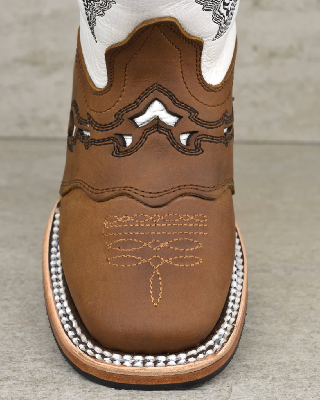 Close-up of a brown cowboy boot with white laces on a gray background