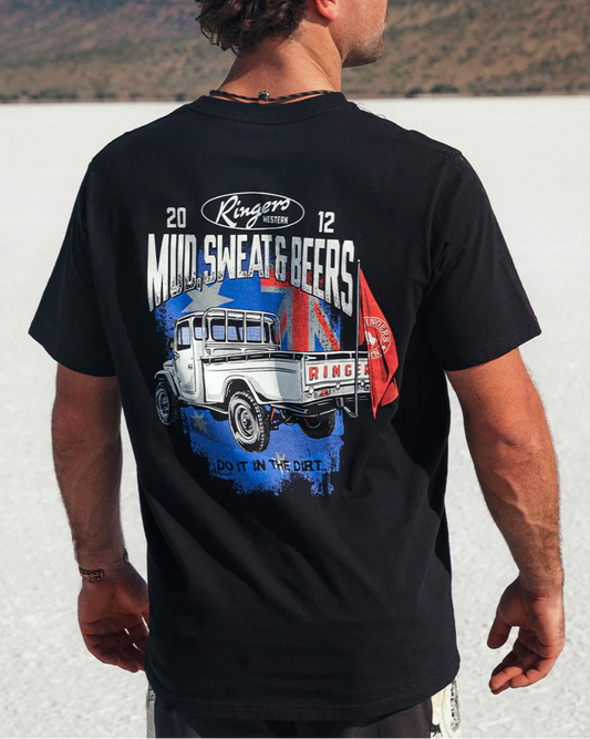 Man wearing a black t-shirt with a graphic design of a truck and text, standing outdoors.