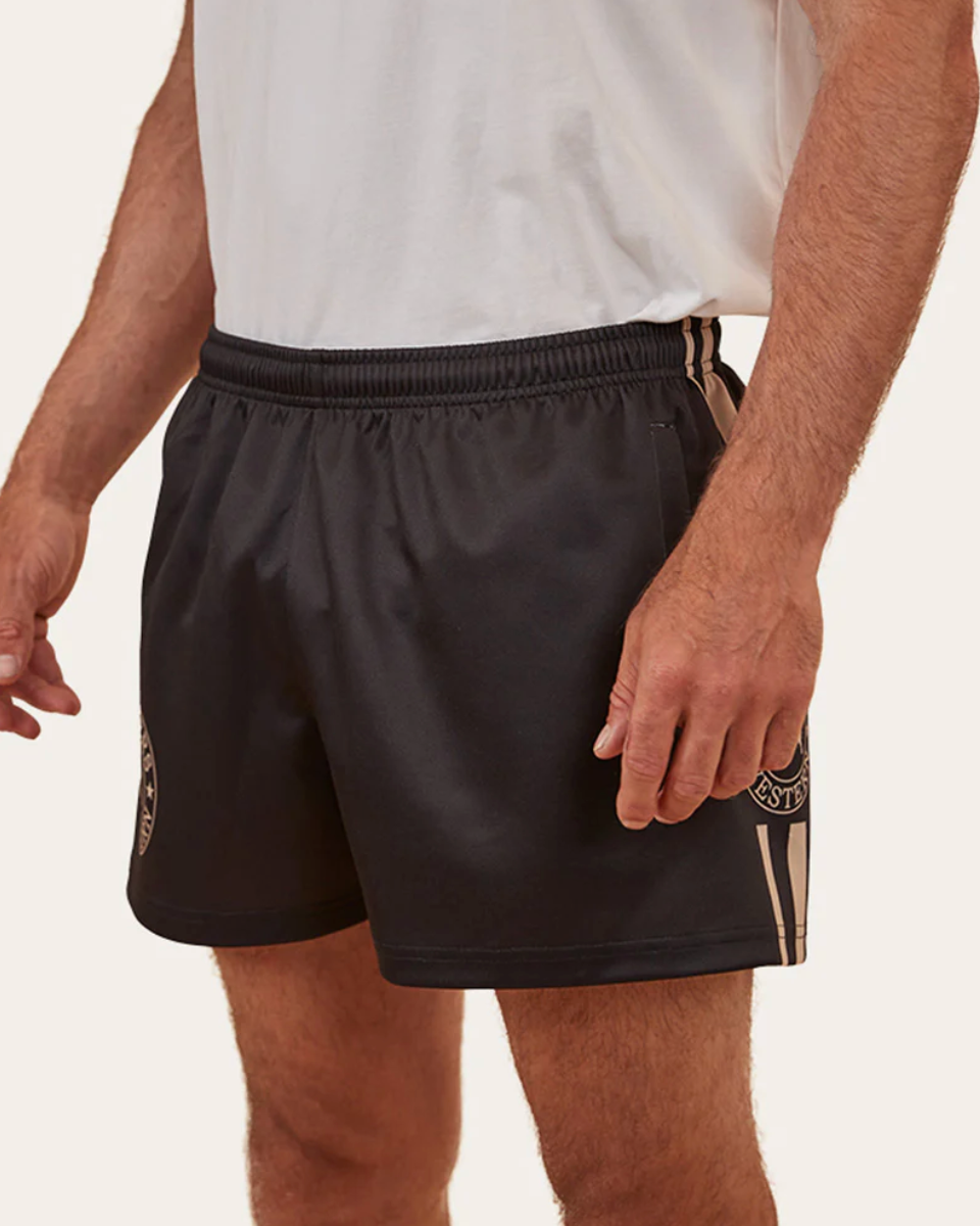 Person wearing black shorts with gold accents on a plain background