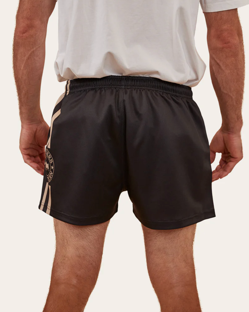 Person wearing black shorts with a brand logo on a plain background