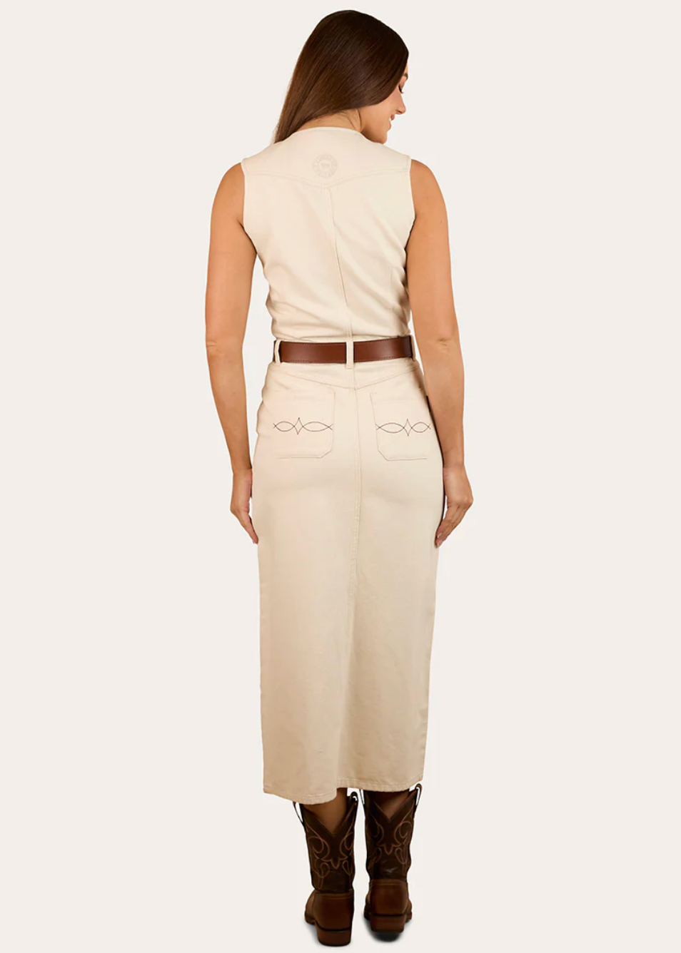Woman wearing a beige dress with a belt and brown boots on a white background