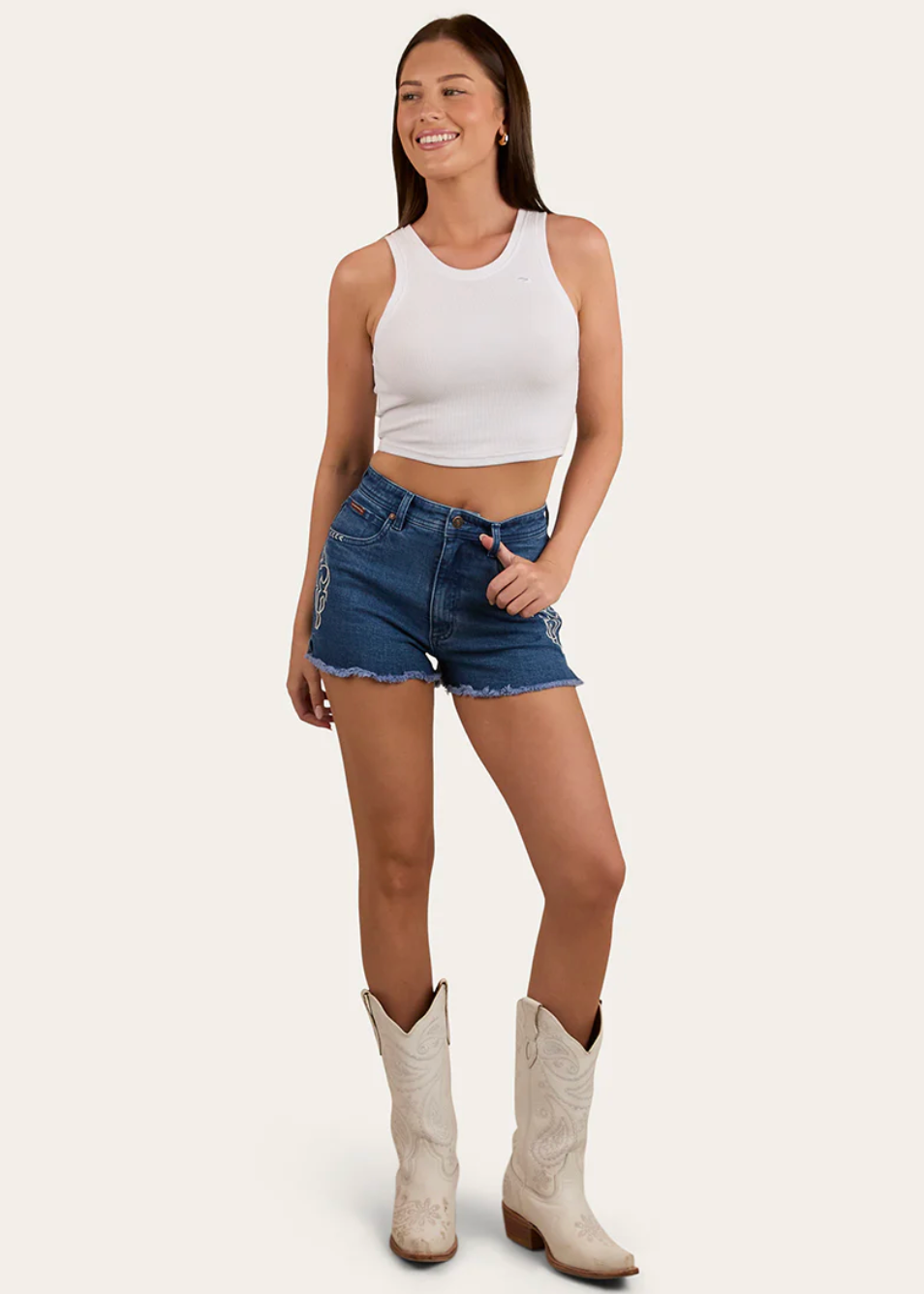 Woman wearing a white tank top, blue denim shorts, and white cowboy boots on a white background
