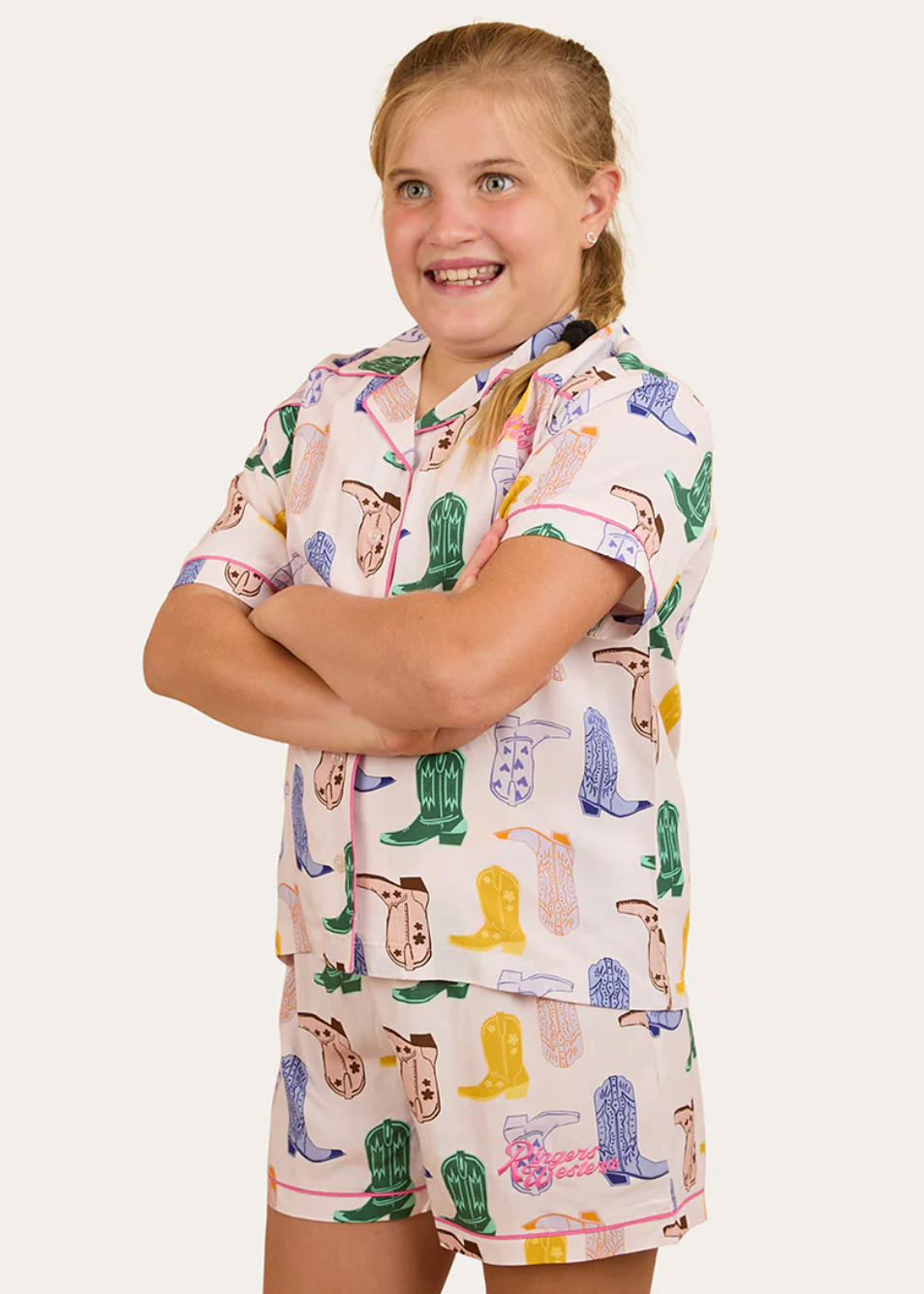 Young girl wearing a pajama set with cowboy boot and hat pattern on a plain background