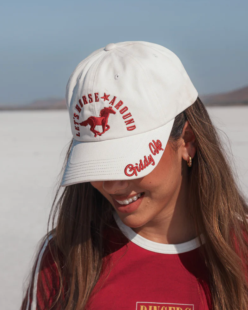 Person wearing a white cap with red text and graphics, standing against a plain background