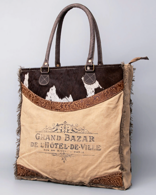 Tote bag with cowhide pattern and 'Grand Bazar de l'Hétel de Ville' branding on a light gray background