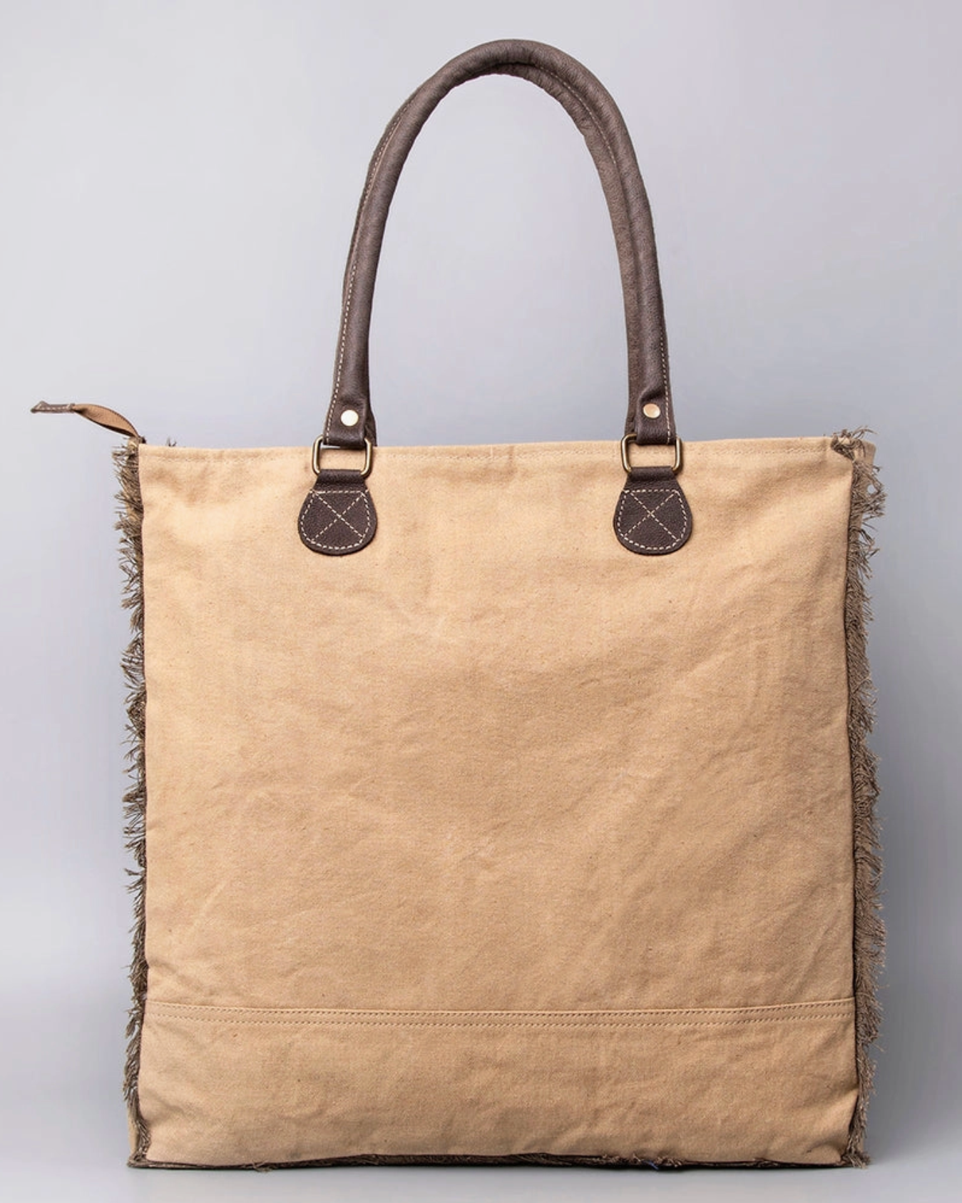 Beige tote bag with brown handles and fringes on a gray background