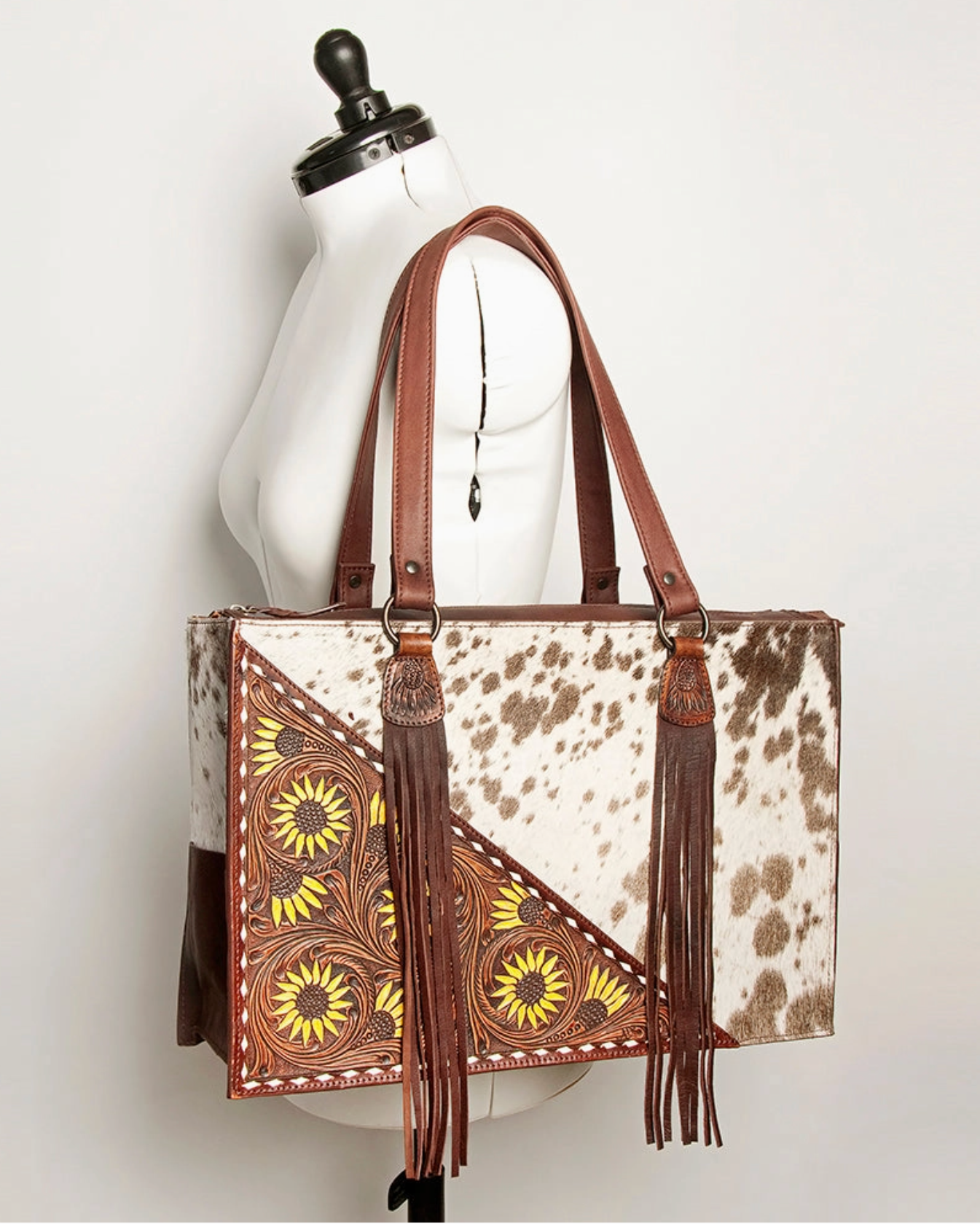 Cowhide patterned handbag with brown leather accents on a mannequin against a white background