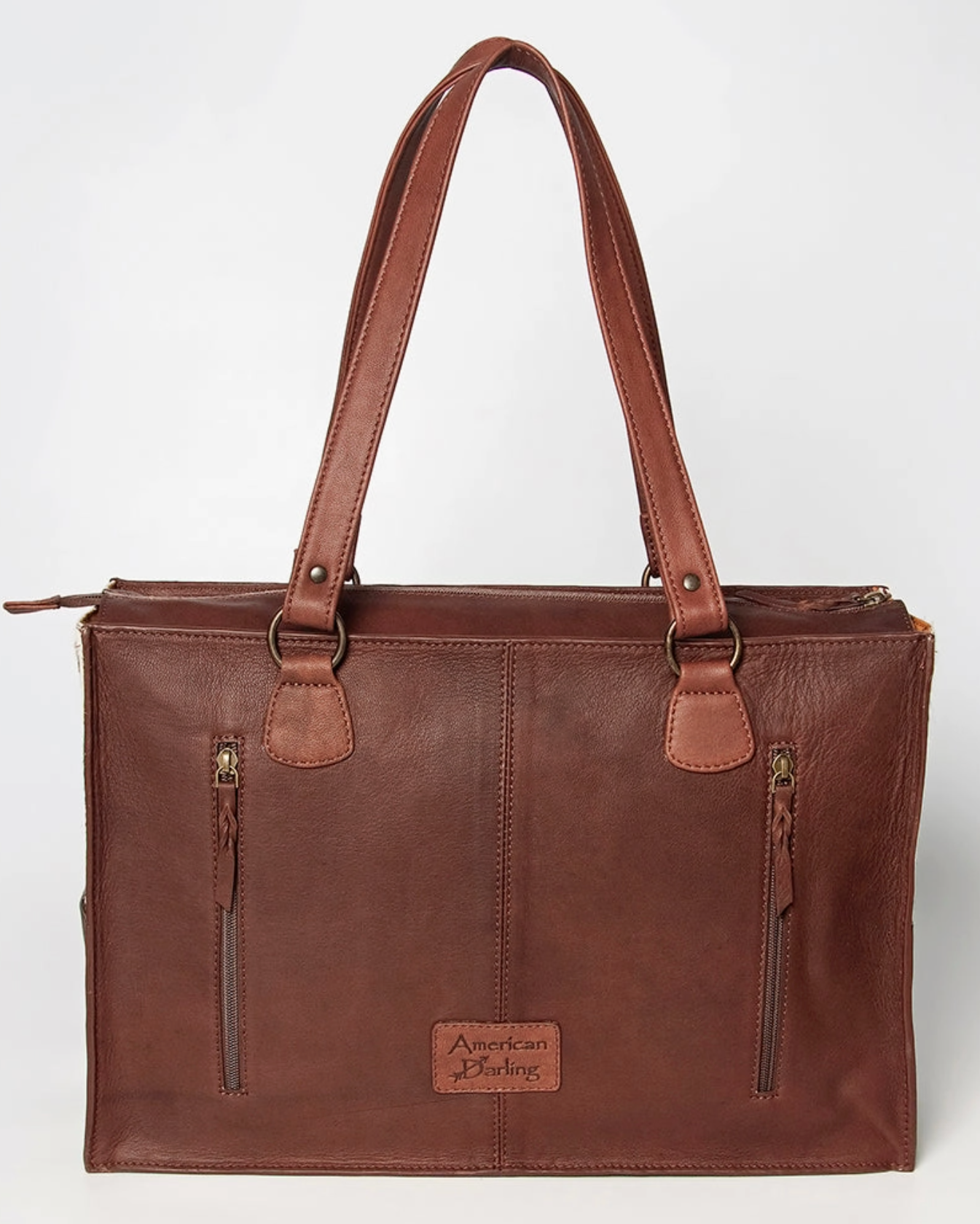 Brown leather tote bag with American Heritage label on a white background